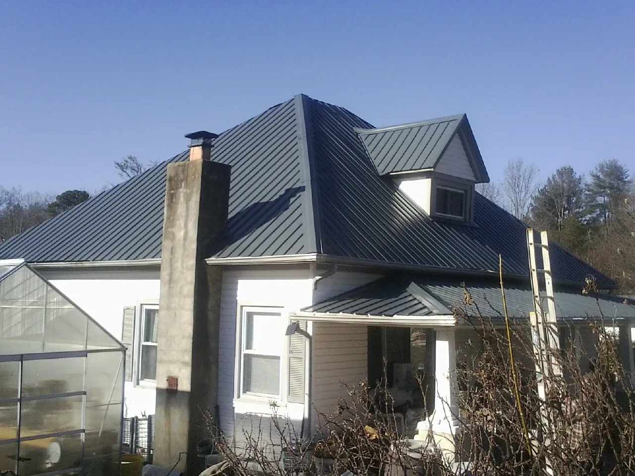 Dark blue standing seam metal roof on a white farmhouse with dormer — Slate & Tile Roof Repair by Roofing Brothers in Huntington Park