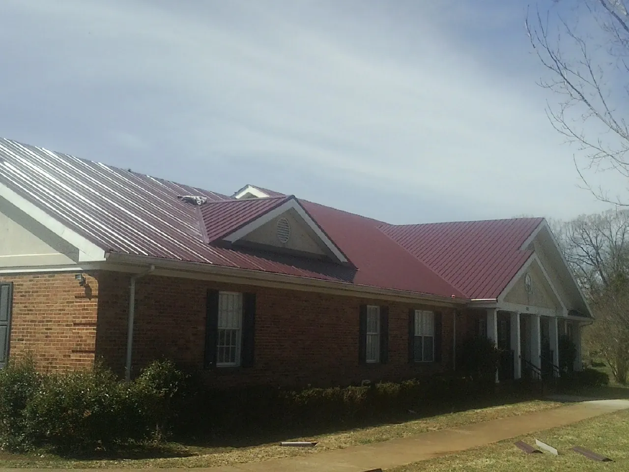 Red metal roof with gabled entries on a long brick building, from a Hail Damage Roof Repair job in Huntington Park