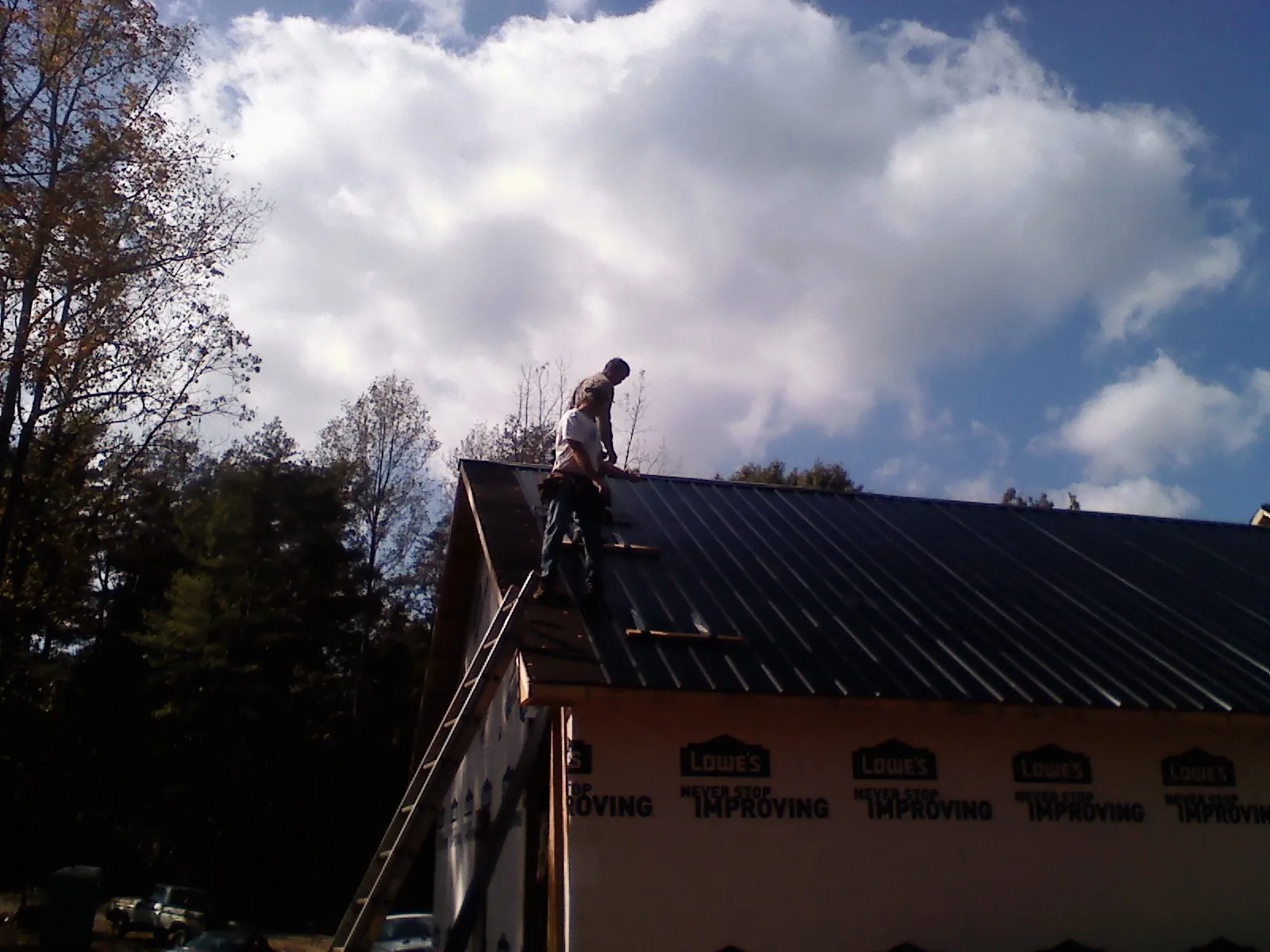 Roofer fastening dark metal panels high against a cloudy sky, from a Roof Inspection job in Huntington Park