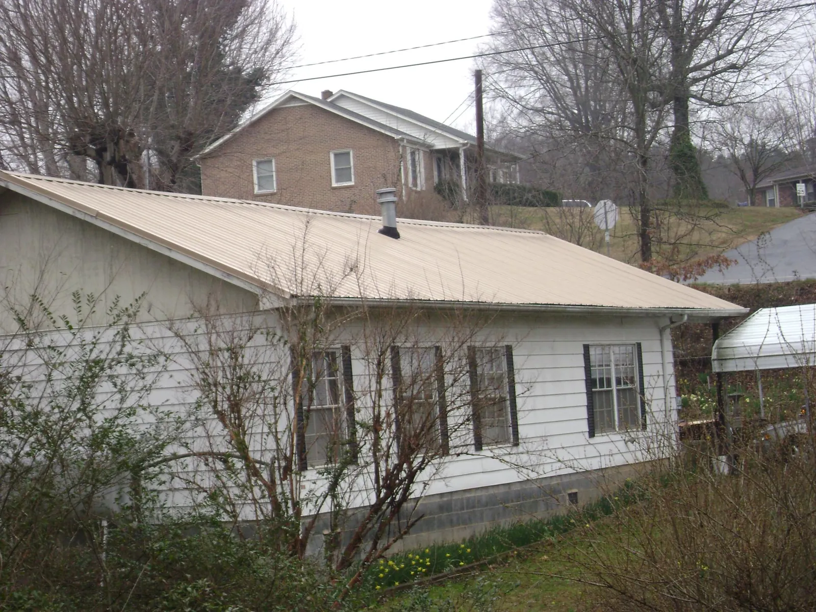 Tan metal roof on a white sided house set into a hillside — Commercial Roofing by Roofing Brothers in Huntington Park